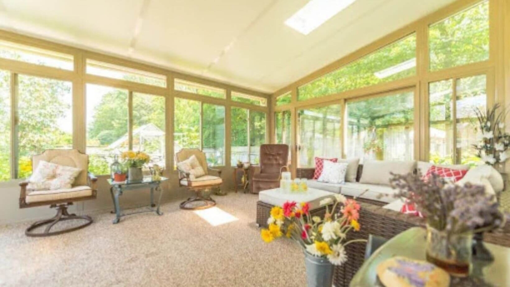 A beautiful 3-season glass sunroom surrounded by lush greenery, providing a perfect blend of indoor comfort and outdoor views.