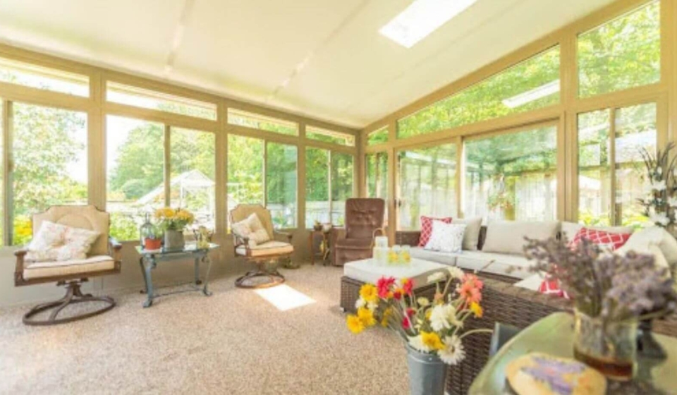 A beautiful 3-season glass sunroom surrounded by lush greenery, providing a perfect blend of indoor comfort and outdoor views.