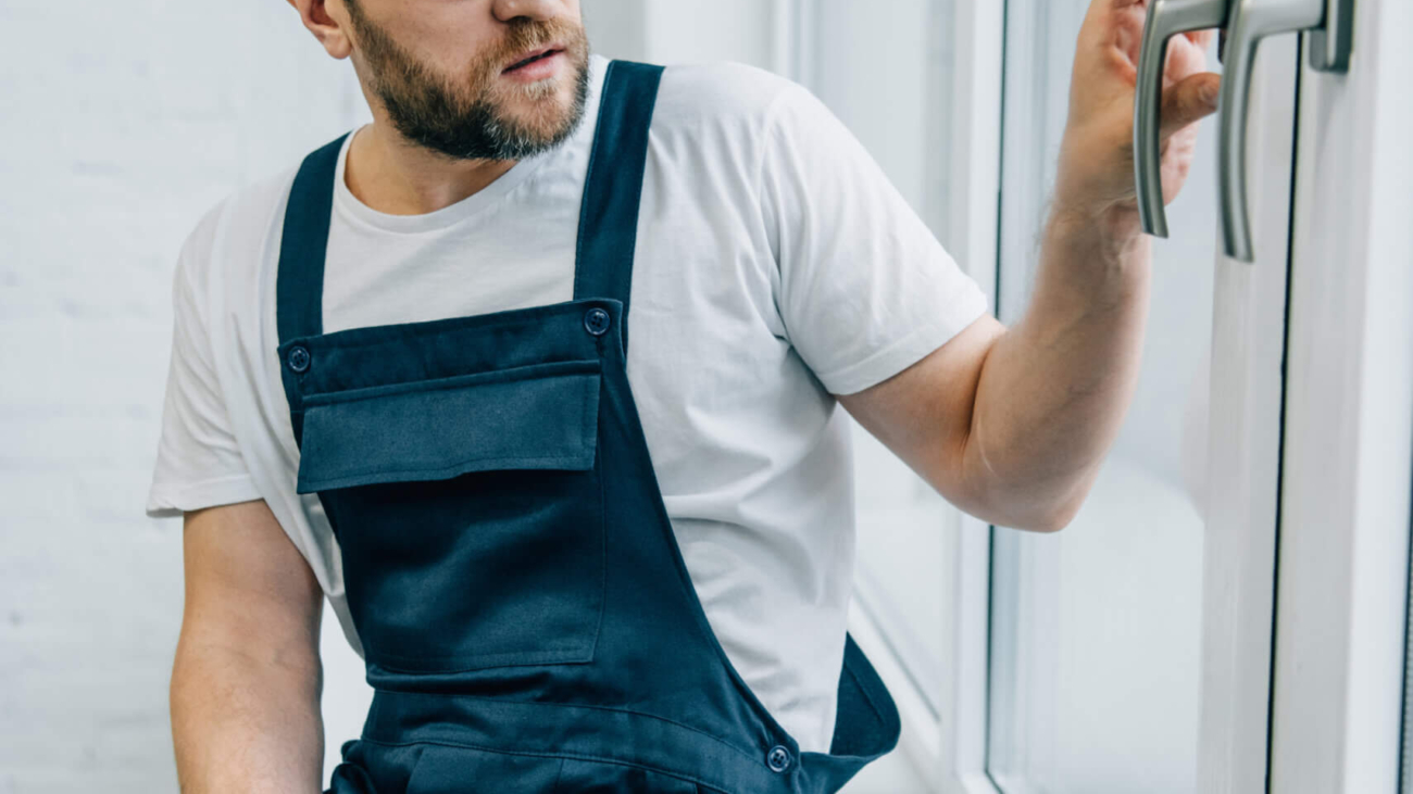 bearded adult repairman in goggles checking window handle